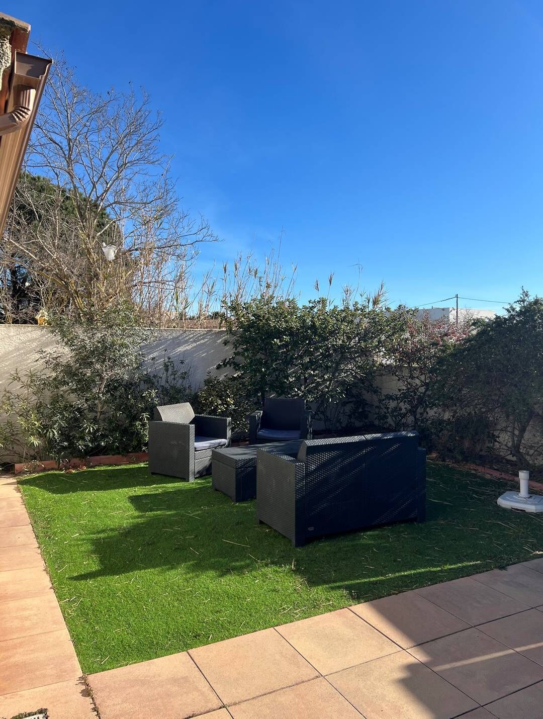 A patio area with outdoor furniture, a well-maintained lawn, and a variety of shrubs and trees.