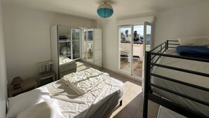 Un dormitorio compacto con una cama individual, una litera, un armario con espejos y una puerta corrediza de vidrio que da a un balcón.