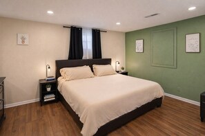 Un dormitorio ordenado con una cama grande, mesitas de noche y una pared verde decorativa.