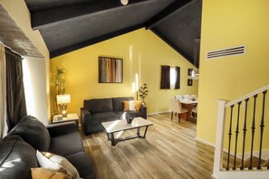 Una sala de estar con un sofá de cuero negro, una mesa de centro blanca y una pared amarilla.
