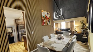 Un comedor moderno con una mesa grande y sillas, una obra de arte contemporánea en la pared y una cocina al fondo.