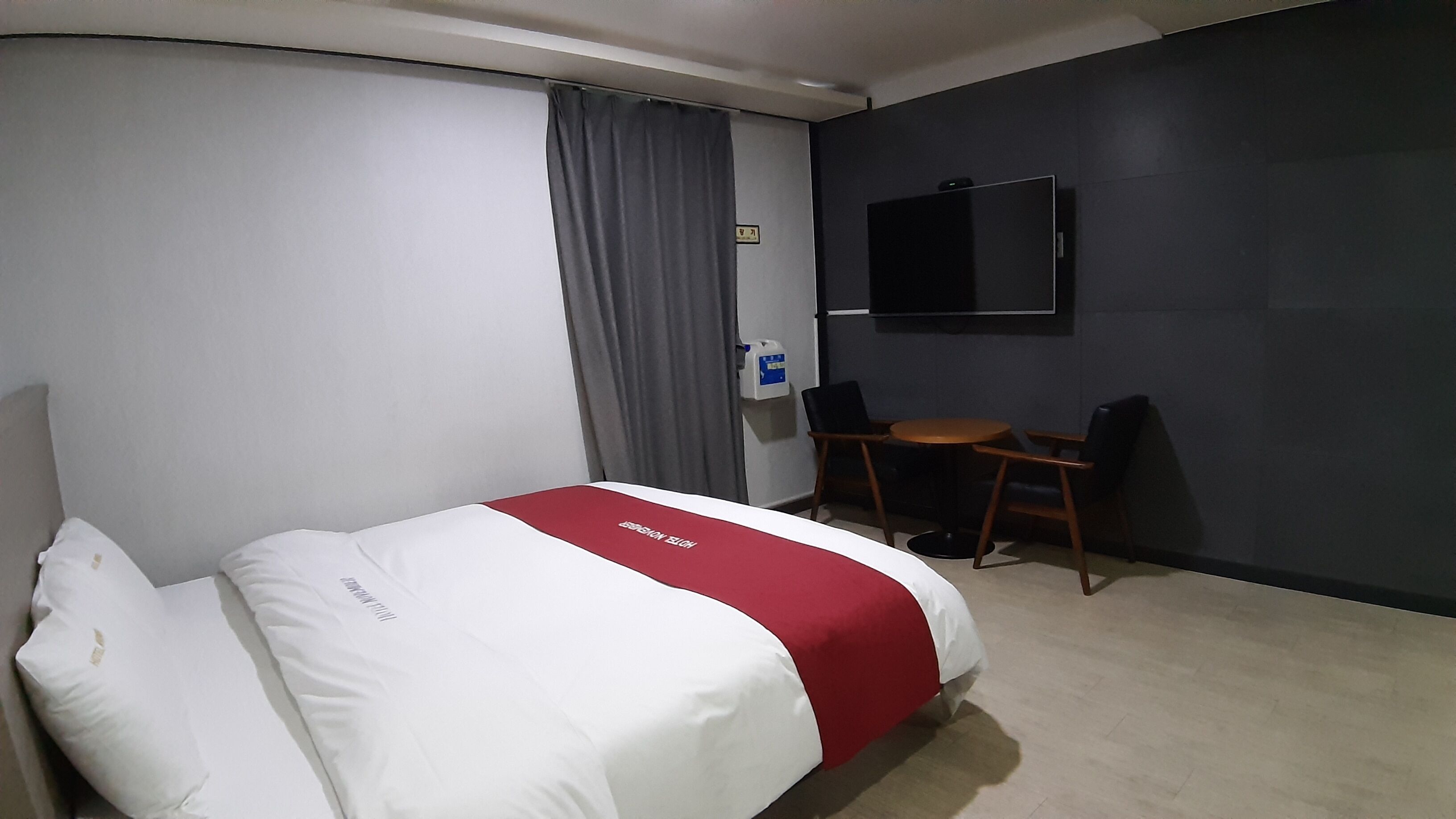 Une chambre d’hôtel avec un lit, un bureau, une chaise, une télévision et une fenêtre avec des rideaux.
