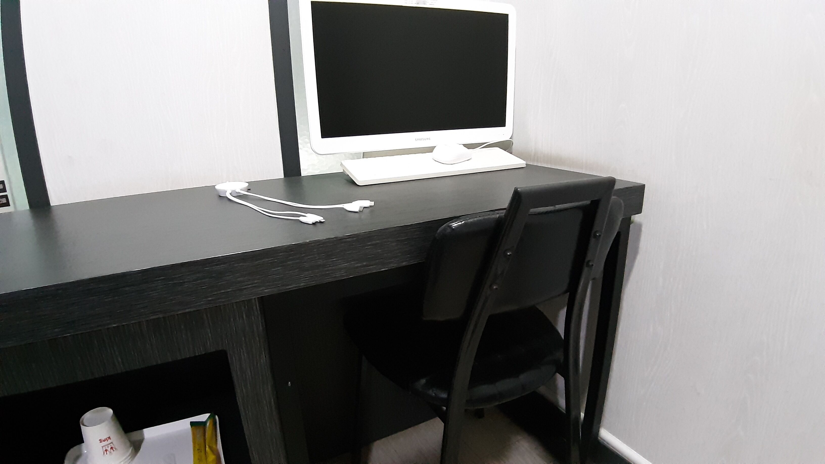 A black desk with a white monitor, a black chair, and a white power strip.