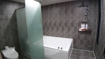A modern bathroom with a glass shower enclosure, a white bathtub, and a shelf with toiletries.