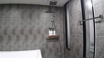 Un baño con paredes de azulejos oscuros, ducha con cabezal de ducha manual y mampara de vidrio.