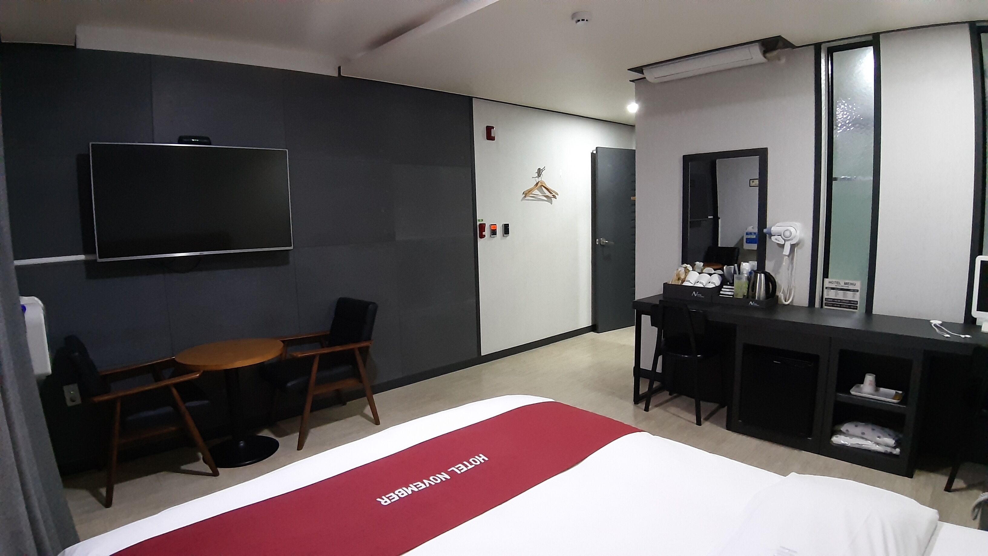 Habitación de hotel con cama, escritorio, silla, televisor, espejo y minibar.
