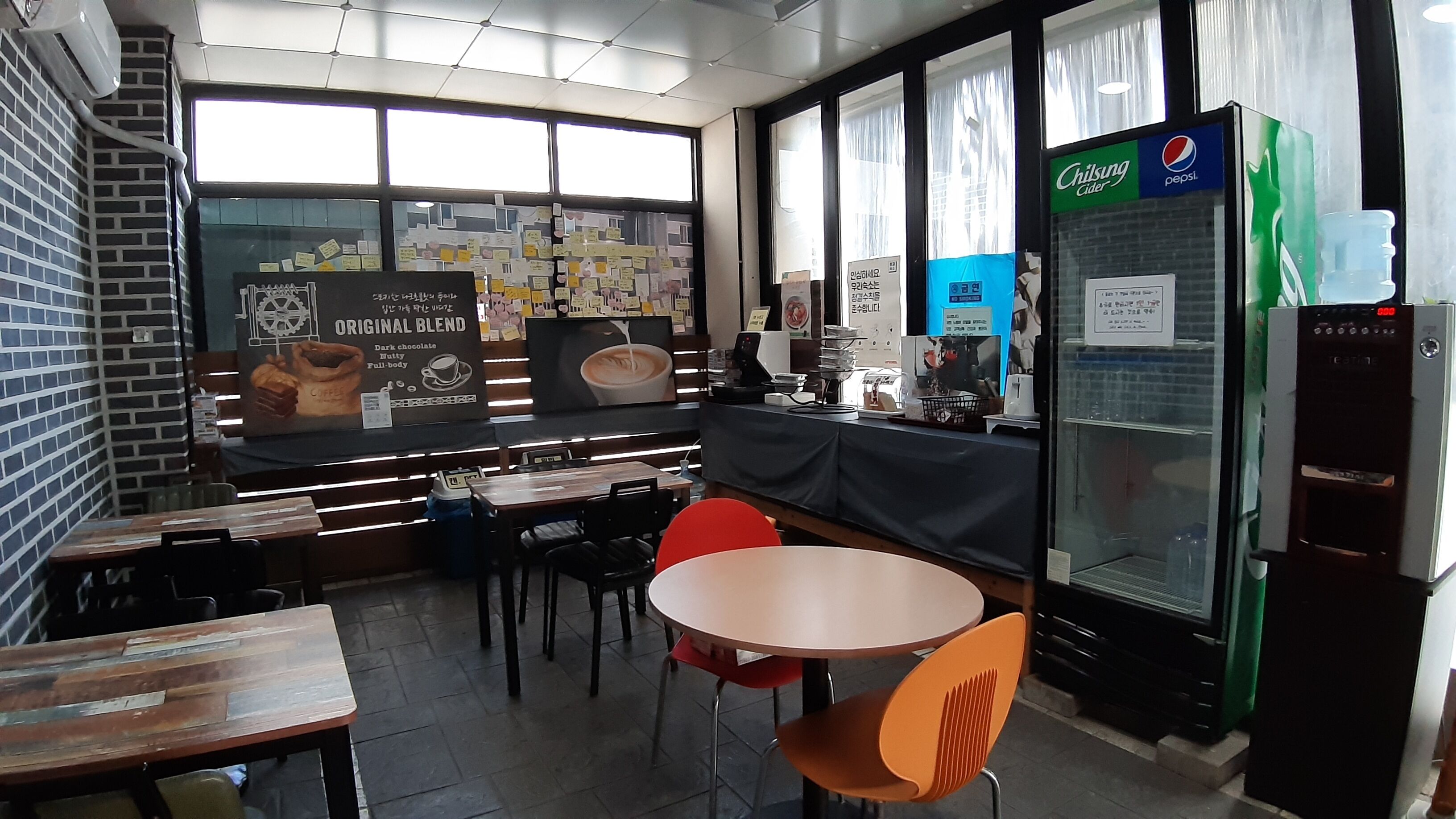 A cafe with tables, chairs, a coffee machine, and a refrigerator with a Pepsi sign.
