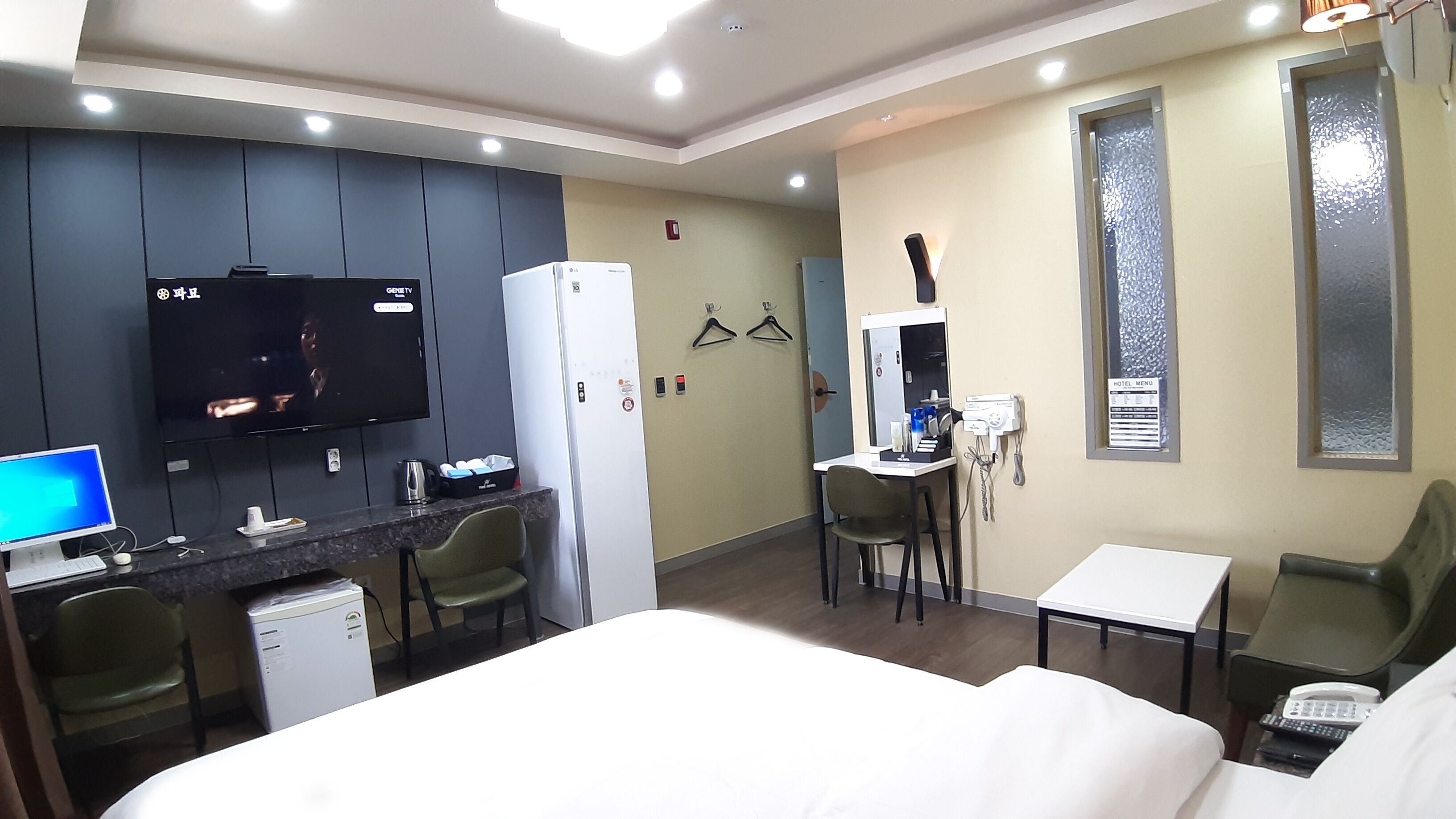 A hotel room with a bed, a desk with a computer, a refrigerator, a TV, and a small kitchenette.