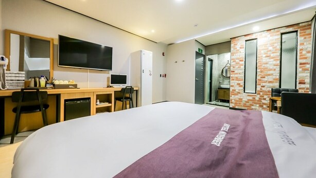 A hotel room with a large bed, a desk with a computer, a TV, and a bathroom visible through an open door. - Seosan November Hotel (Seosan)