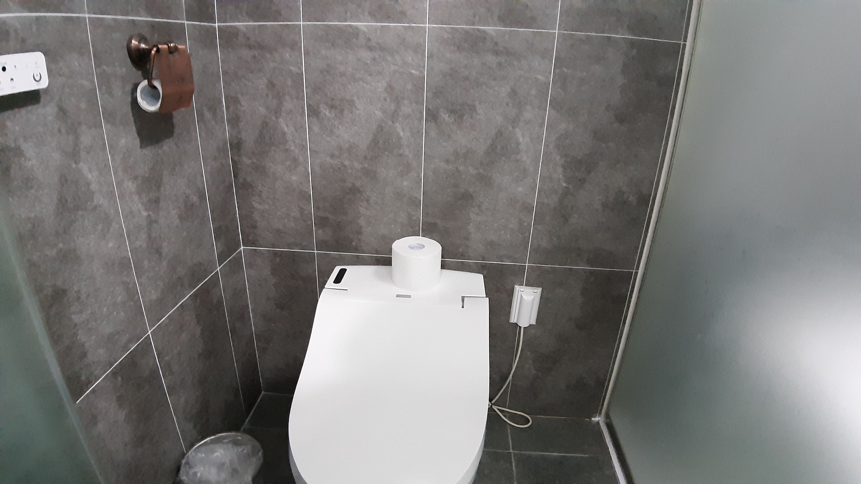 A small, tiled bathroom with a toilet, a paper towel dispenser, and a hand dryer.
