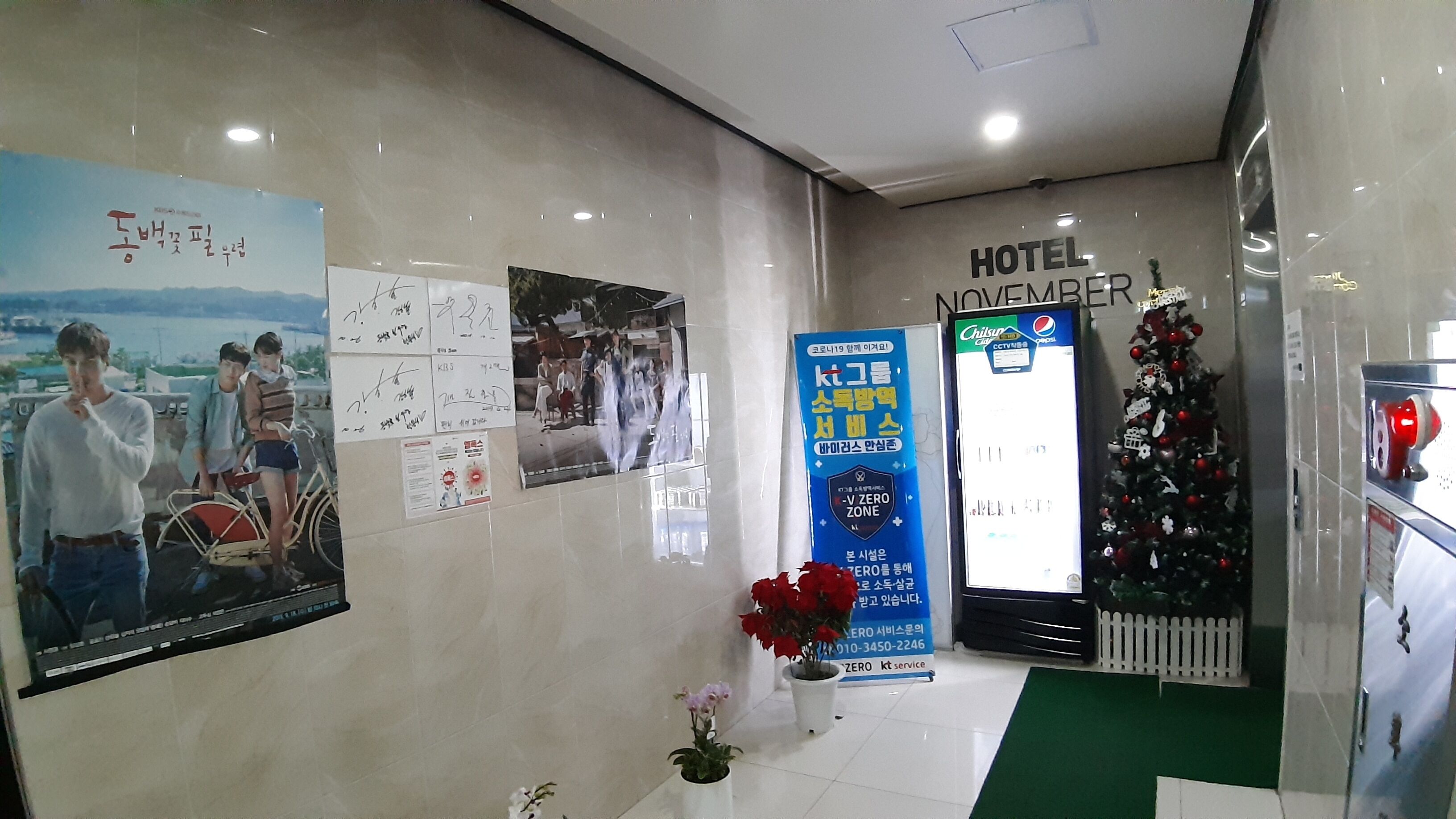 A hotel lobby with a reception desk, a Christmas tree, and various posters on the walls.