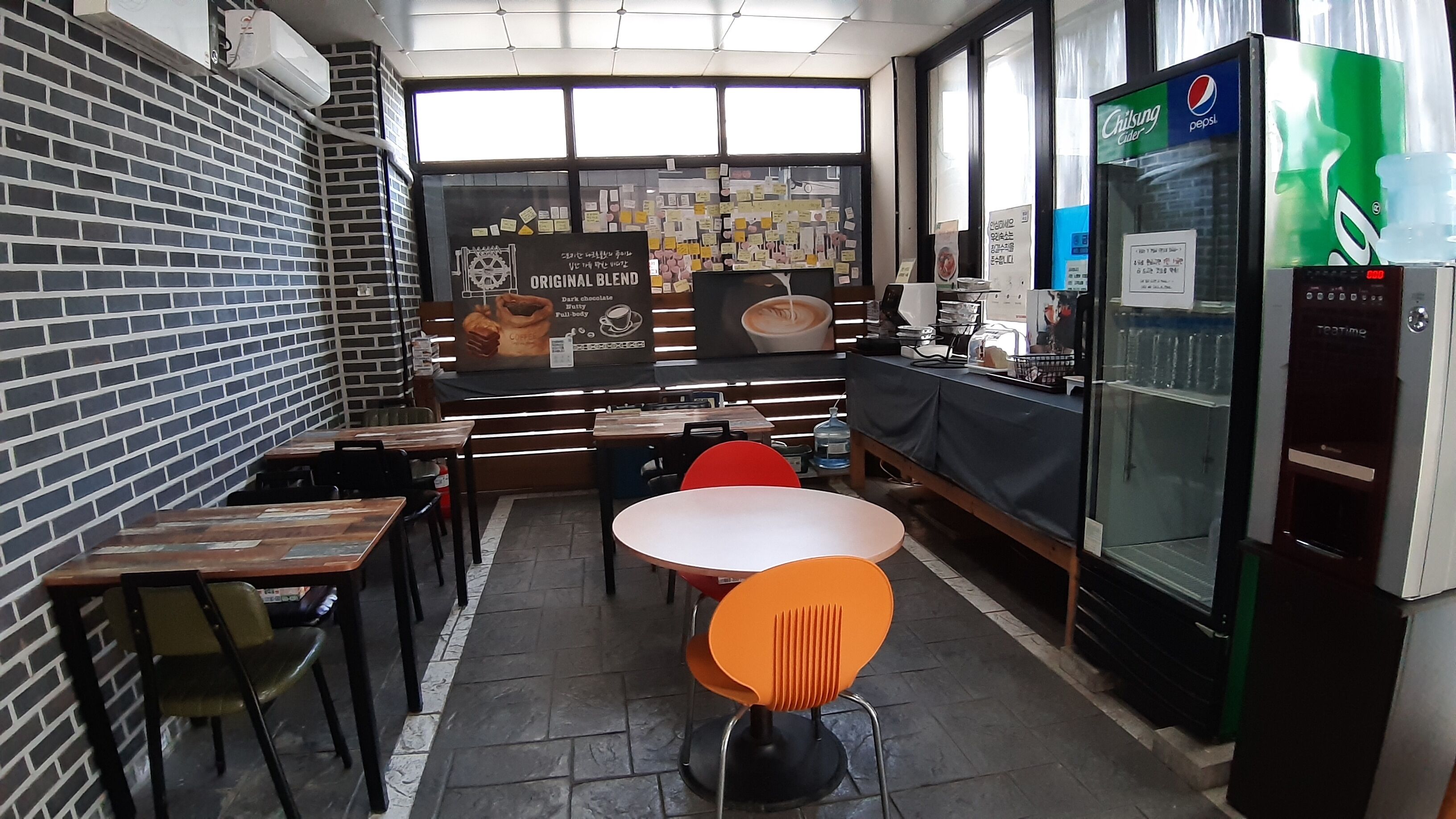 Ett kafé med tegelväggar, träbord och orange stolar.