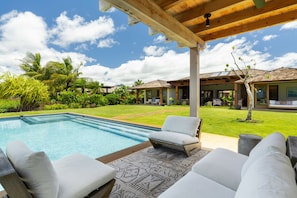 A poolside area with a wooden pergola, outdoor seating, and a view of a residential property with a covered patio and a lawn. - Hale Kipu by Alekona Kauai: Luxury 5br Ocean View Home w Pool, Fire pit, Spa (Koloa)