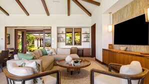 A spacious living room with a large sectional sofa, two armchairs, a coffee table, and a TV mounted on a wooden wall. - Hale Kipu by Alekona Kauai: Luxury 5br Ocean View Home w Pool, Fire pit, Spa (Koloa)