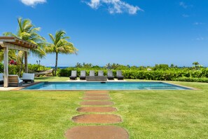 A swimming pool with a clear view of the ocean, surrounded by a well-maintained lawn and palm trees.