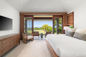 A bedroom with a large bed, a TV, a wooden dresser, and a view of a pool and garden.
