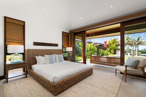 A spacious bedroom with a large bed, a sitting area with a chair, and a view of a tropical garden through large windows. - Hale Kipu by Alekona Kauai: Luxury 5br Ocean View Home w Pool, Fire pit, Spa (Koloa)