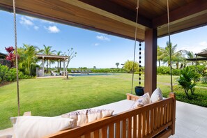 A wooden swing bed with a view of a pool and garden.