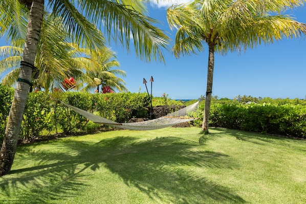 A hammock in a lush garden with palm trees and a view of the ocean. - Hale Kipu by Alekona Kauai: Luxury 5br Ocean View Home w Pool, Fire pit, Spa (Koloa)
