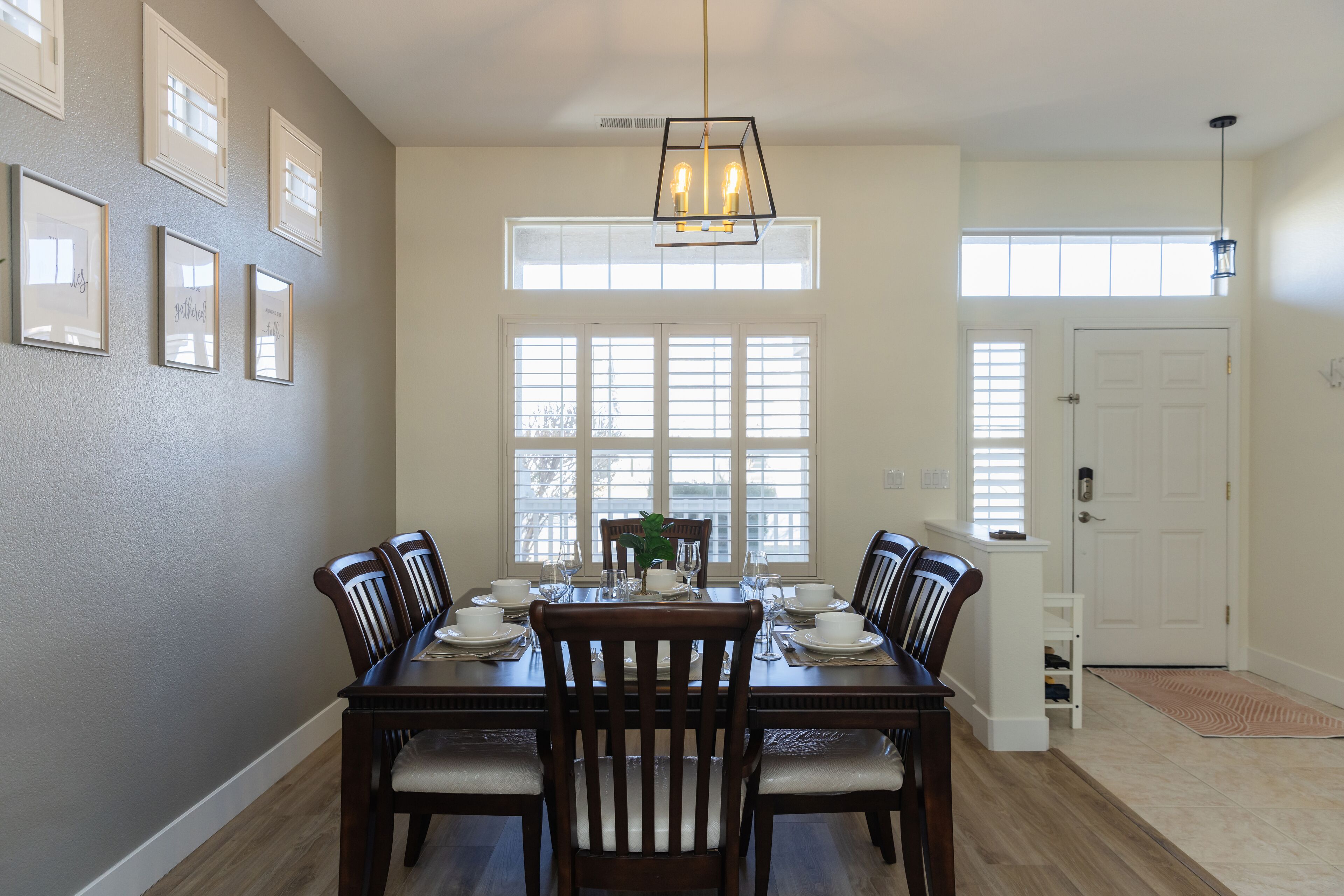 A dining room with a wooden table set for six, flanked by chairs, a chandelier, and framed pictures on the wall.