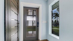 Un hall d’entrée moderne avec une porte sombre, un tapis à motifs et une fenêtre dotée d’un grillage métallique.