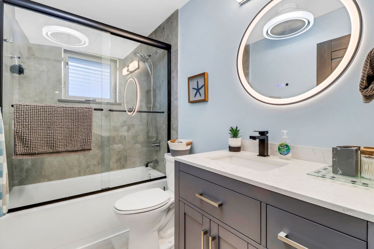 Een moderne badkamer met een douche met glazen wand, een ronde spiegel en een witte wastafel.