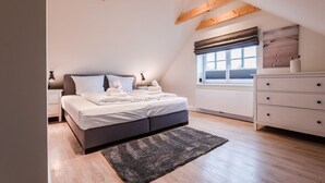 Un dormitorio moderno con cama, mesitas de noche, cómoda, ventana con vistas y vigas de madera a la vista.