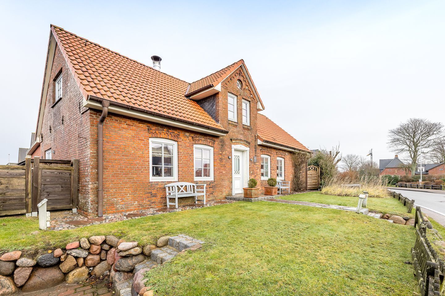 A two-story brick house with a tiled roof, a front porch, and a stone wall border.
