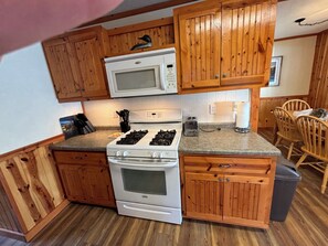 Una cocina compacta con armarios de madera, un microondas, una estufa a gas y un tostador.