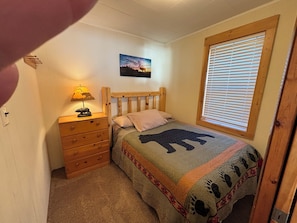 Un dormitorio con una cama de madera, una mesita de noche, una lámpara, una ventana con persianas y un cuadro colgado en la pared.