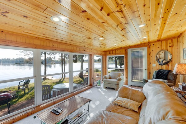 A cabin with a wooden interior, large windows, a sofa, a table, and a grill outside. - Musky Point 3 (Mercer)