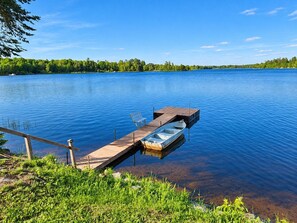 A calm lake with a wooden dock extending into the water, a small boat moored at the dock, and a bench on the dock.