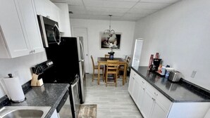 Una cucina moderna con mobili bianchi, un frigorifero nero, un forno a microonde e un'area pranzo con un tavolo e sedie in legno.