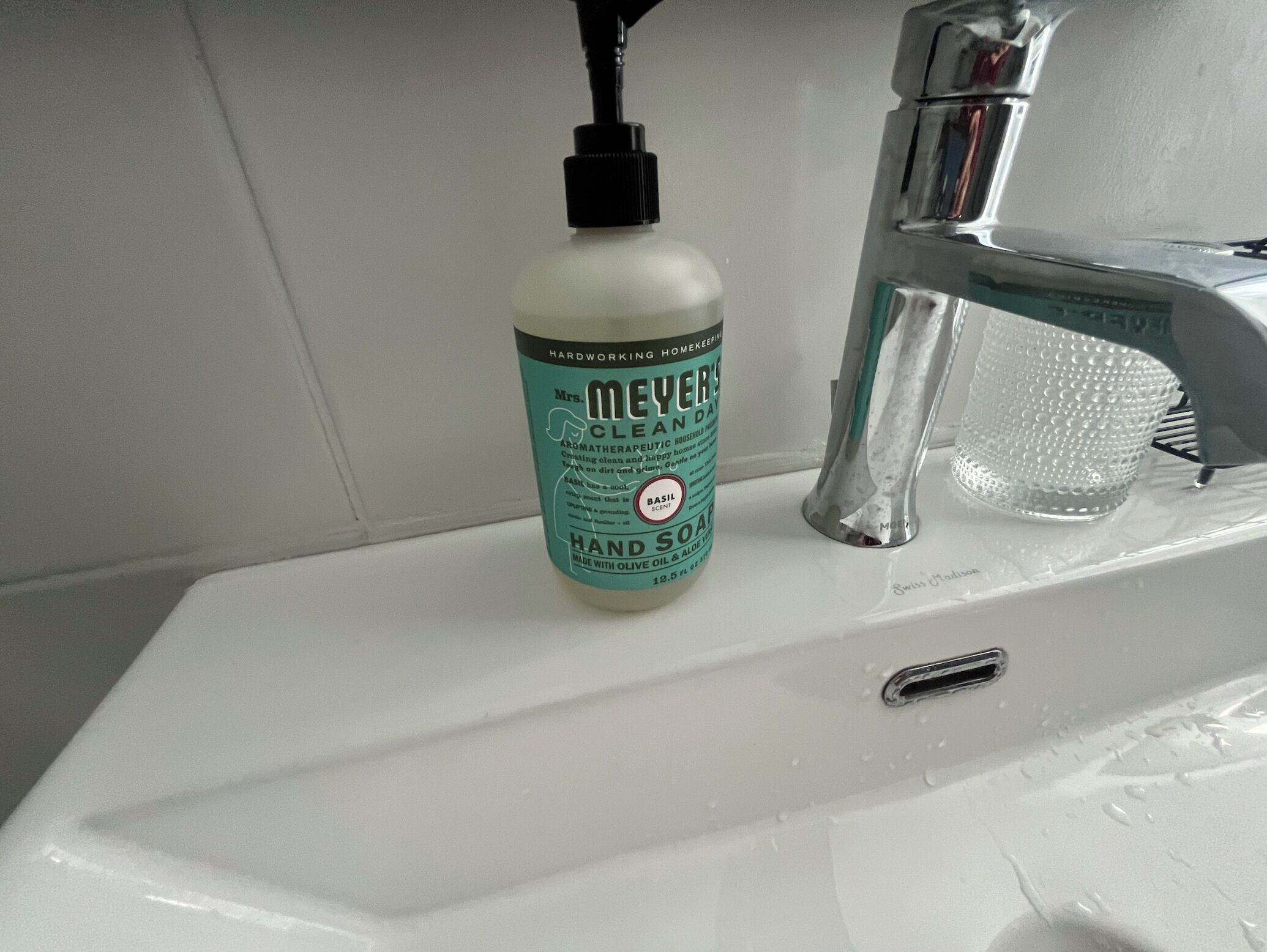 Un lavamanos de baño con una botella de jabón para manos Mrs. Meyer's Clean Day y un grifo moderno.