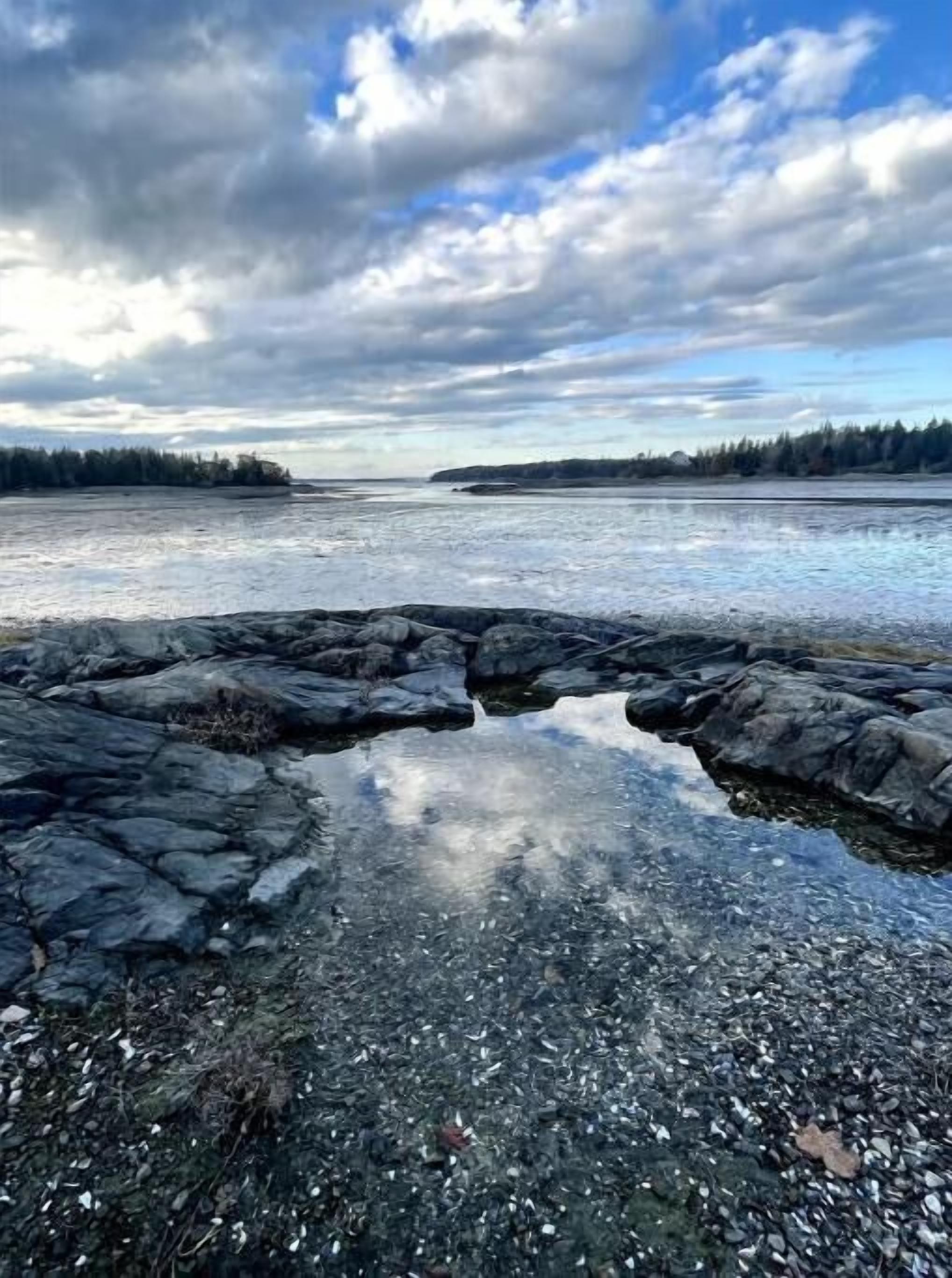 A rocky shoreline with clear water reflecting the sky.