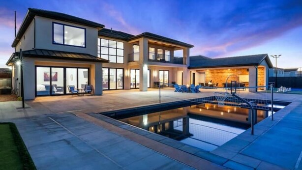 Une maison moderne à deux étages, dotée d’une piscine, de grandes fenêtres et d’un espace extérieur bien éclairé.