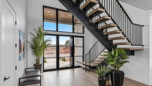 Un intérieur moderne avec un escalier, de grandes fenêtres et des plantes en pot.
