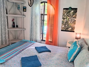 Quarto com cama, prateleira, janela com cortinas e uma obra de arte na parede.