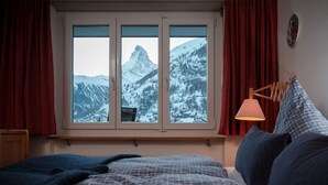 Une chambre à coucher avec un lit, une fenêtre donnant sur des montagnes enneigées, des rideaux rouges et une lampe de chevet.