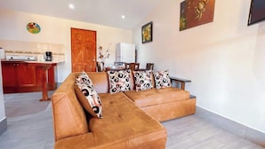 A living room with a brown sofa, patterned cushions, a dining table with chairs, a kitchen area, and a TV mounted on the wall. - Villa Banano 09, Near to the beach with Pool (Jacó)