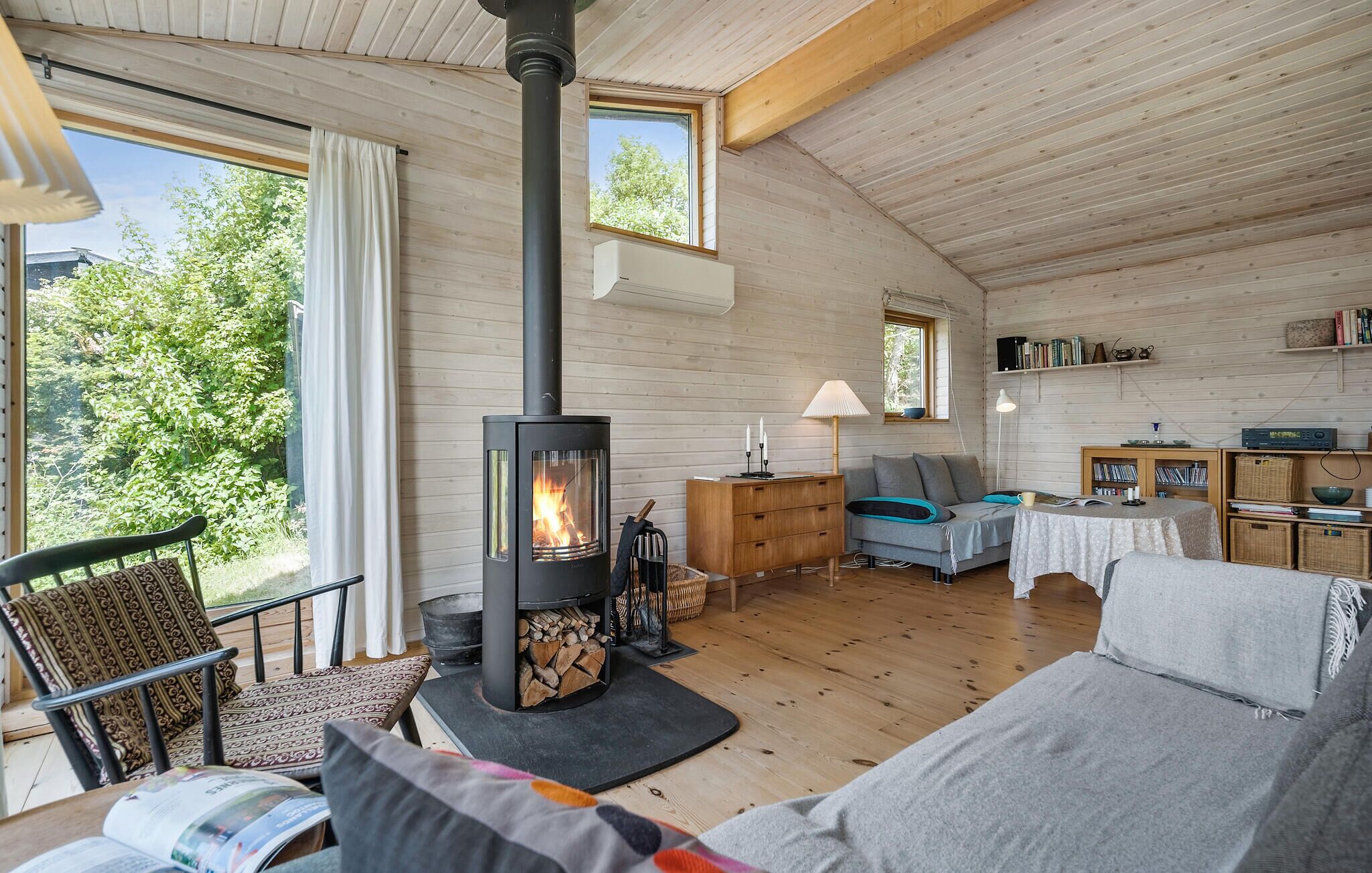 L’intérieur chaleureux d’un chalet avec un poêle à bois, un canapé, une table et une bibliothèque.