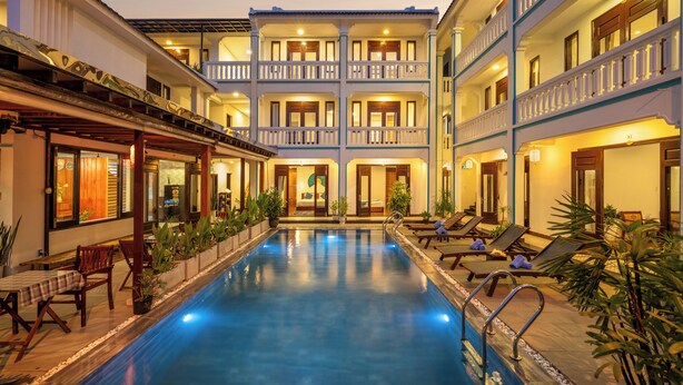 A hotel with a central pool, multiple balconies, and outdoor seating areas.