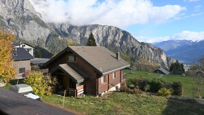 A wooden cabin with a sloped roof, surrounded by a grassy area and mountains in the background. - Kil-Ukru by Interhome (Ovronnaz)