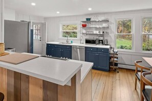 Une cuisine moderne dotée d’un îlot central, d’appareils électroménagers intégrés et offrant une vue sur l’extérieur.
