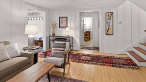Un salon comprenant un canapé, un fauteuil, une table basse, une lampe, une table d’appoint, un tapis et un escalier.