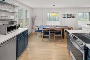Una cocina moderna con armarios blancos, una mesa de comedor de madera y un ventanal grande.