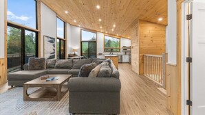 Un interior moderno con techo de madera, ventanas amplias, un sofá, una mesa de centro y una zona de cocina.