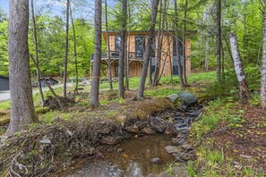 Une cabane dans une forêt, avec un ruisseau et une terrasse en bois.