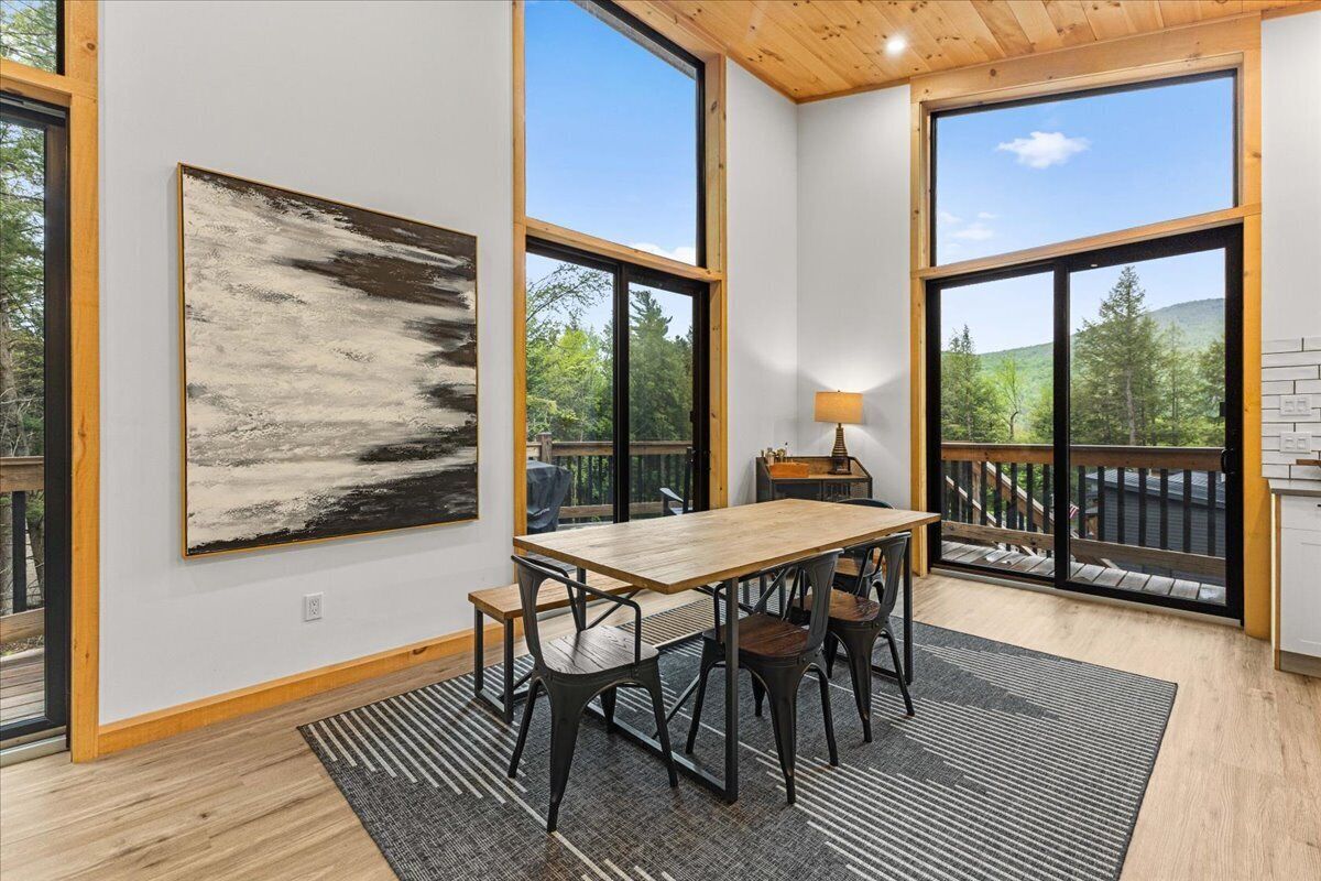 A dining area with a wooden table and chairs, large windows, and a view of trees.