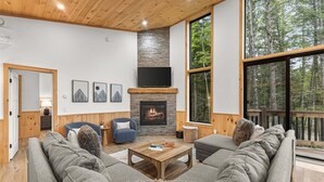Un salón acogedor con chimenea, ventanas amplias y vistas al bosque.